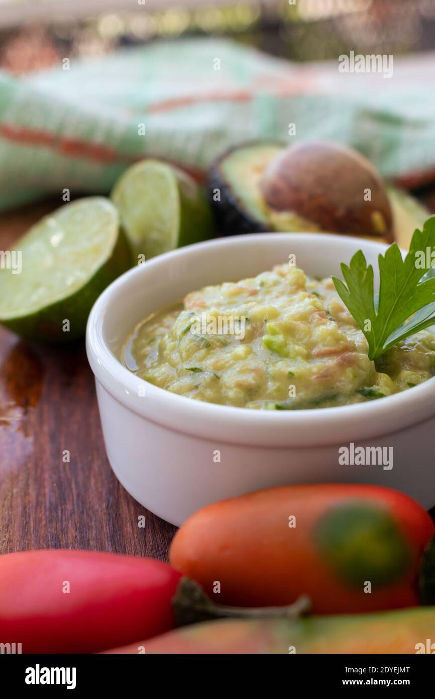 Half an avocado, some hot peppers and a lime on a wooden board and bowl with the guacamole sauce. Stock Photo