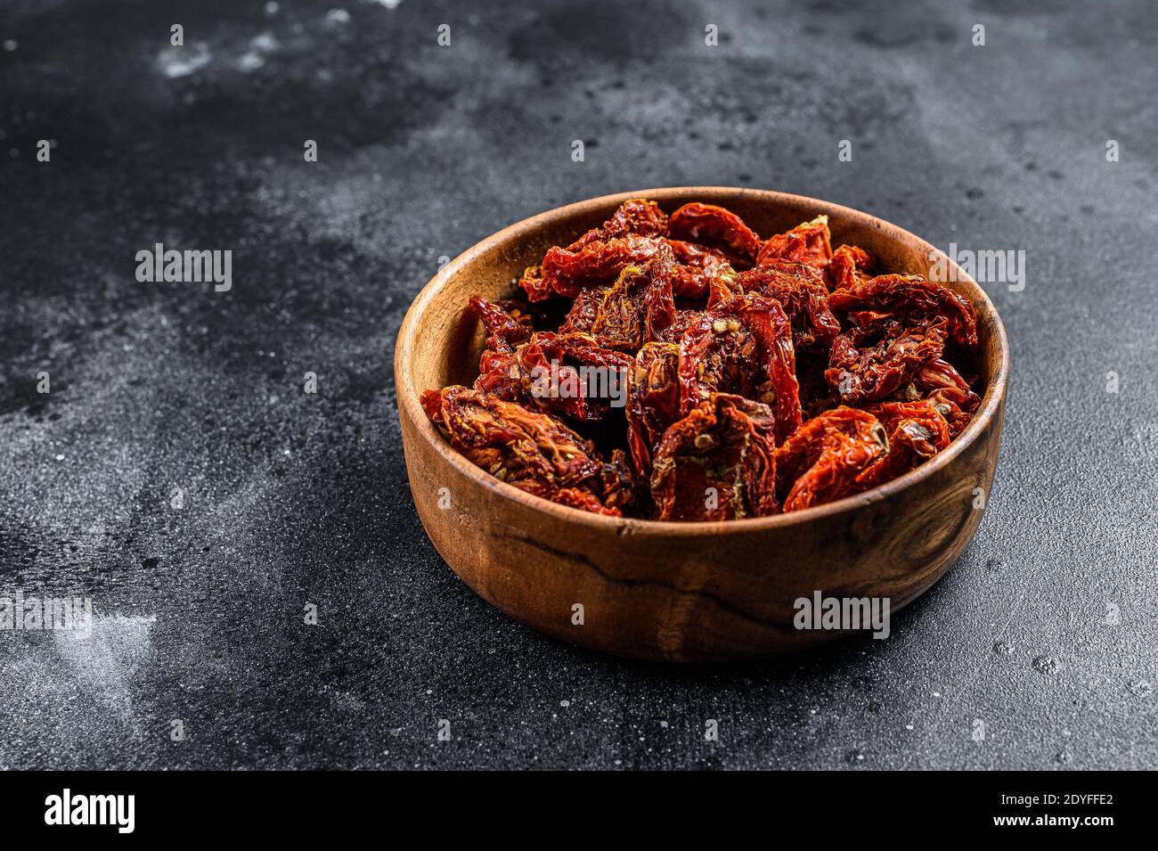 Sun dried tomatoes in wooden bowl. Black, dark background. Top view