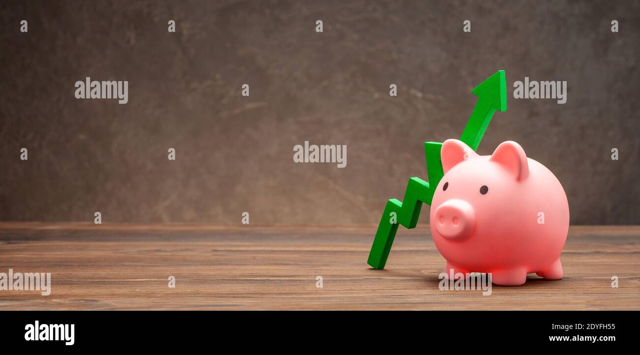 Green up arrow and piggy bank on brown background. Copy space for text ...