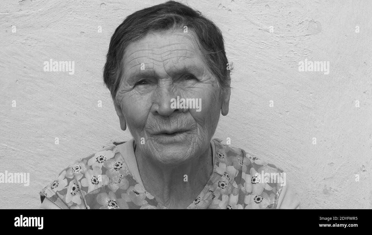 Black and white authentic portrait of 80 years old lady of mixed ethnicity. Wrinkled face of elderly woman with concerned emotion and suspicious sight Stock Photo