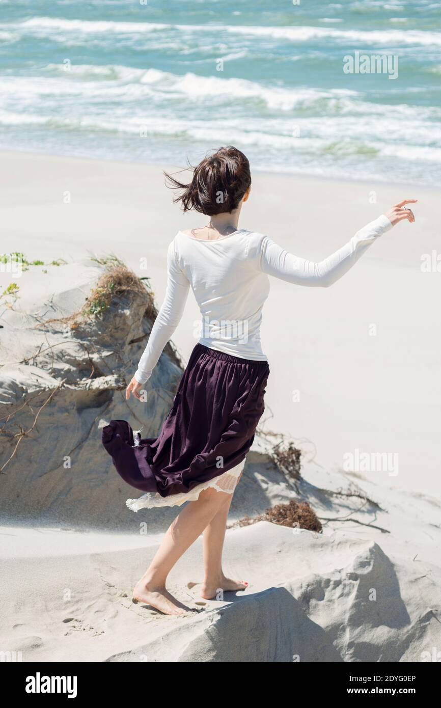 Beautiful brunette woman in a long dress walks along the seashore Stock ...