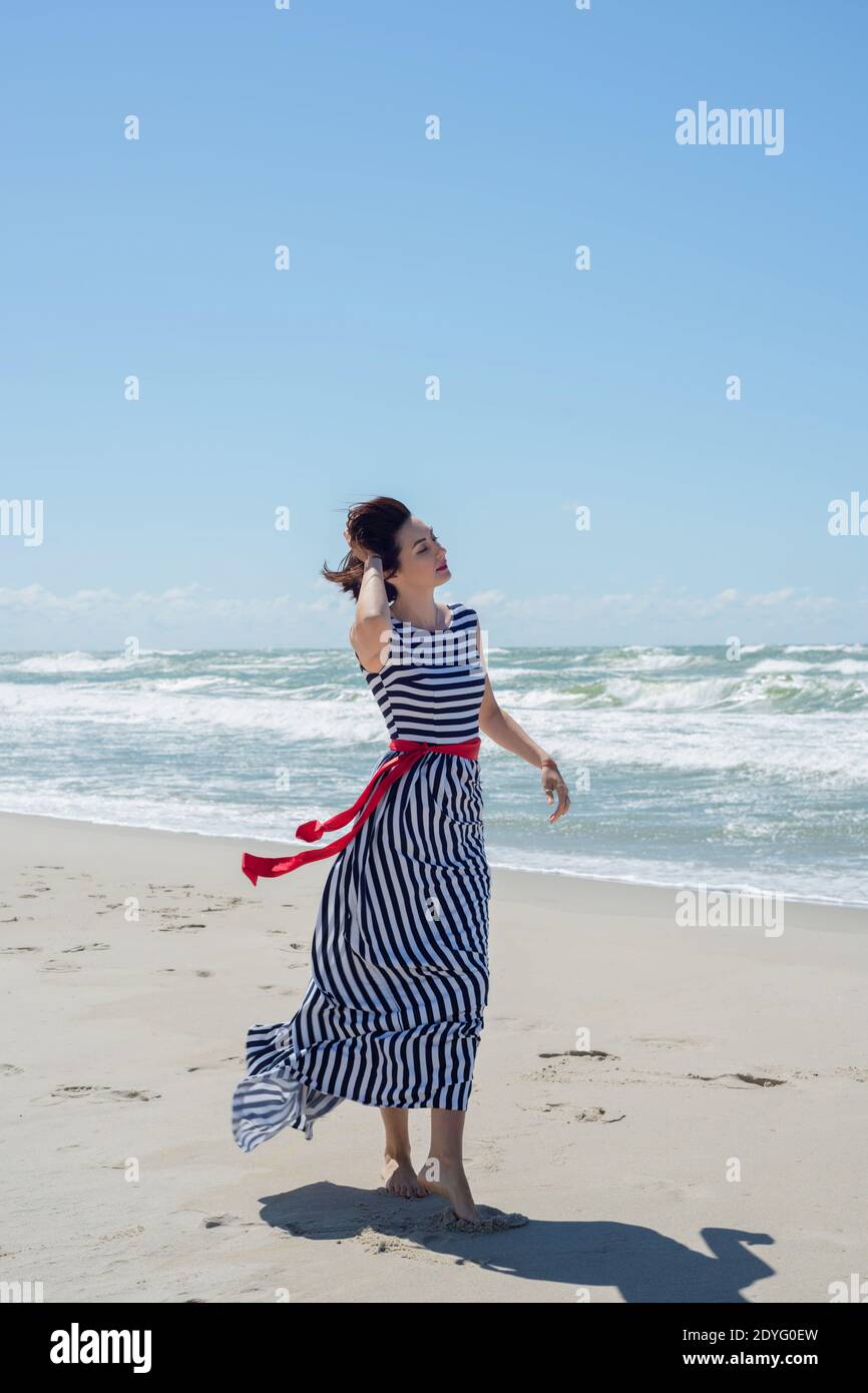 Beautiful brunette woman in a long dress walks along the seashore Stock ...