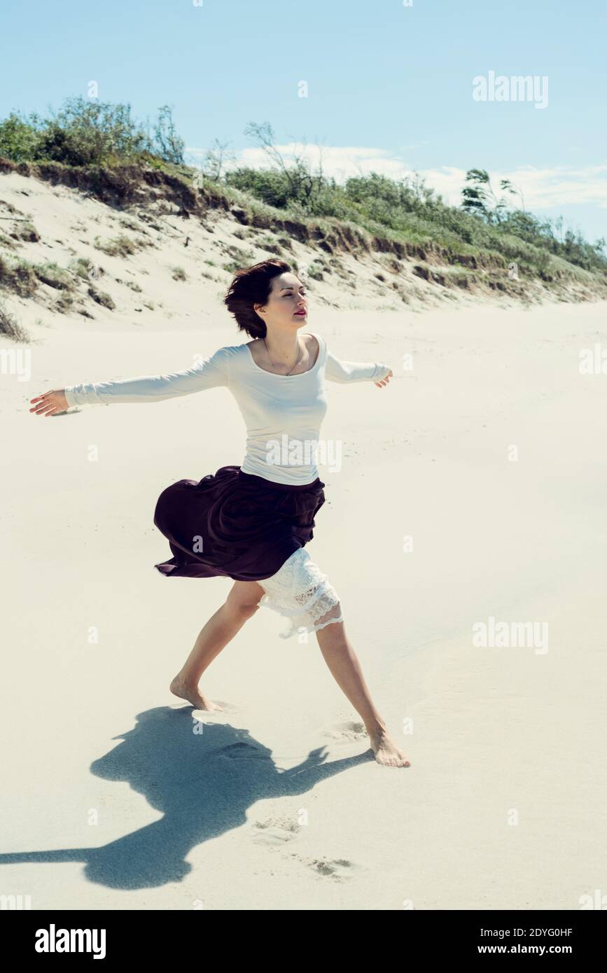 Beautiful brunette woman in a long dress walking along the seashore ...