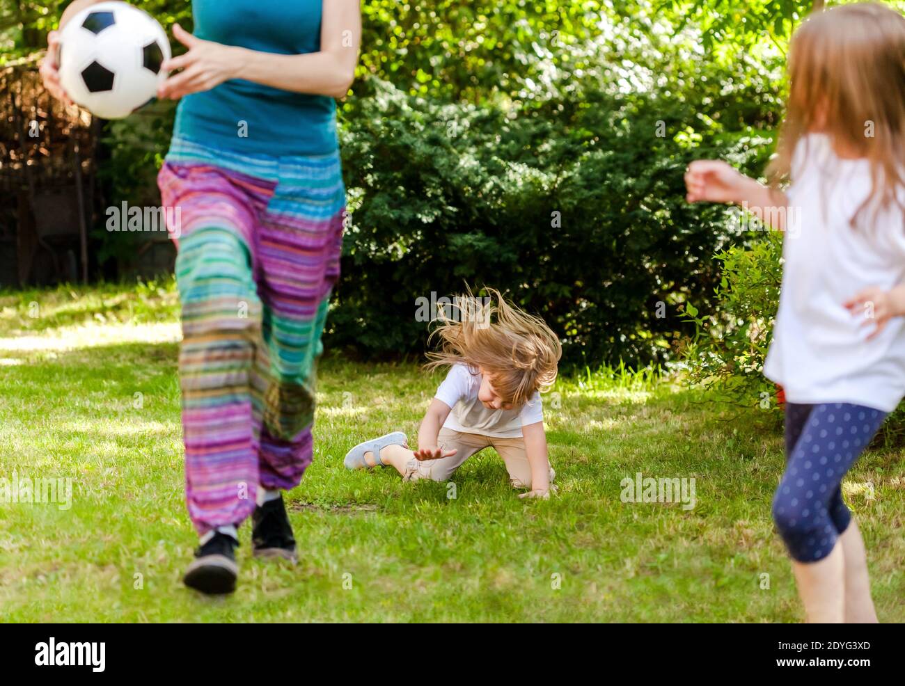 Child falling down running, playing ball with family in the garden, injury concept. Kids outdoors sport activity accident, fall on the grass Stock Photo
