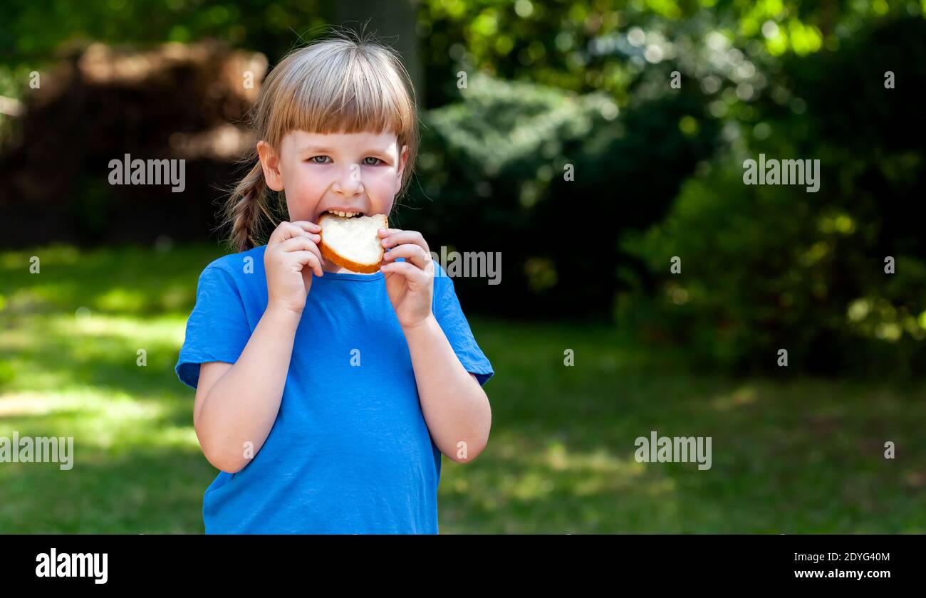 Child, one little girl eating a plain slice of bread with butter in the garden outside, closeup, portrait Single person, school age kid eating bread Stock Photo