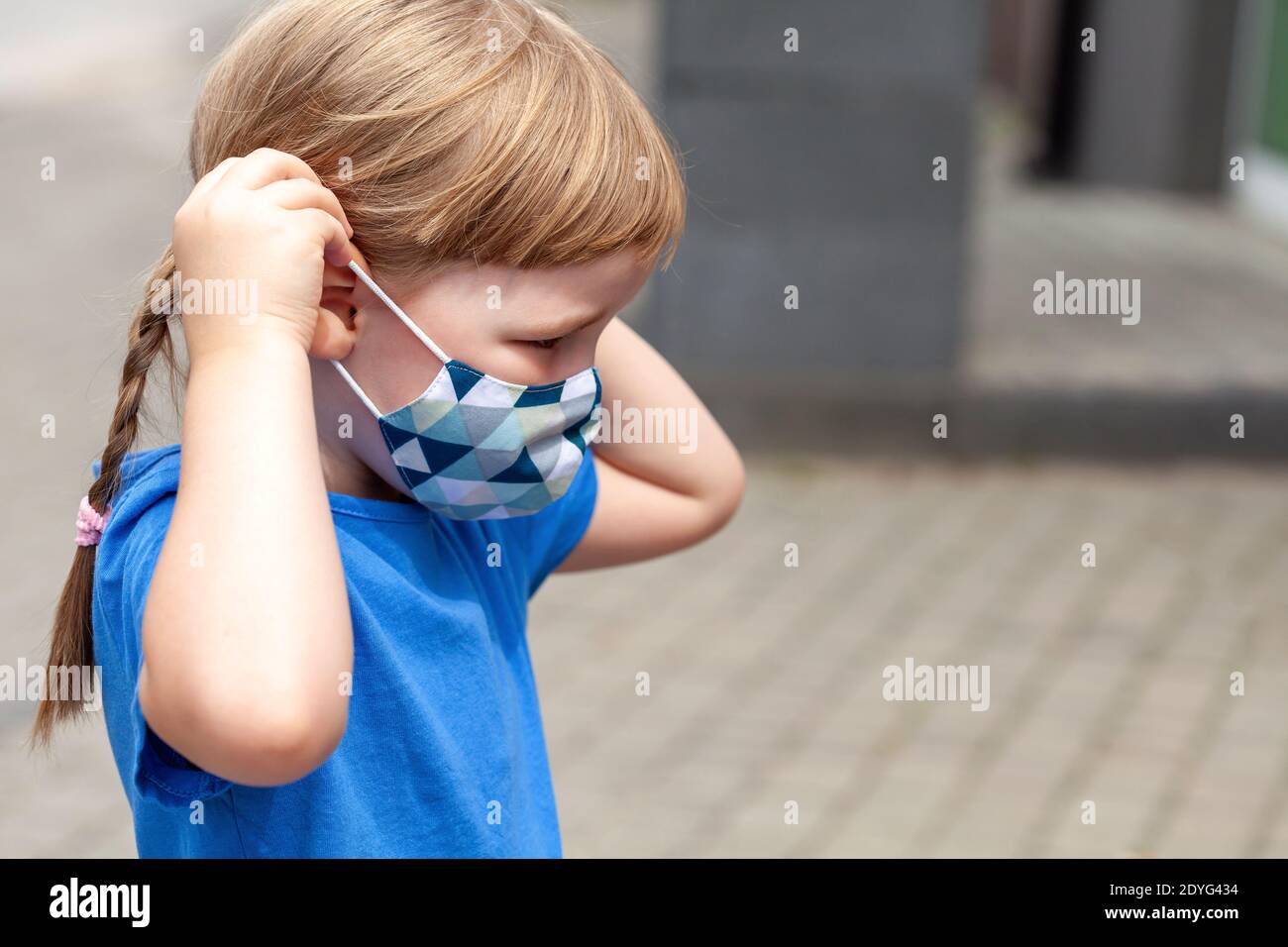 Lone little child, school age girl putting on or taking off her anti viral face mask, portrait, closeup, copy space Covid 19, corona virus pandemic Stock Photo