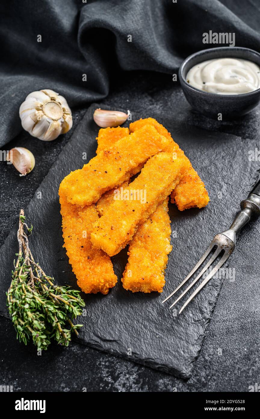 Oven baked crumbed fish sticks made from white fish. Black background