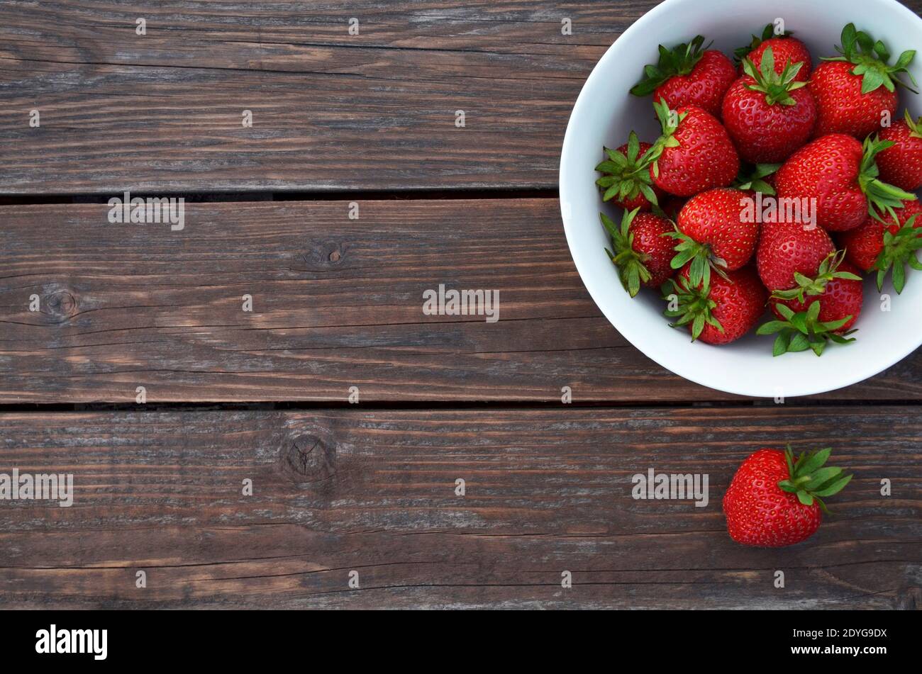 Fresh red strawberries in a white bowl on a old wooden table close-up with copy space, top view. Healthy eating concept. Stock Photo