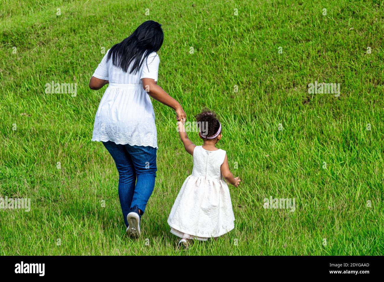 Afro-Caribbean mother and daughter walking in a lawn, Cuba Stock Photo