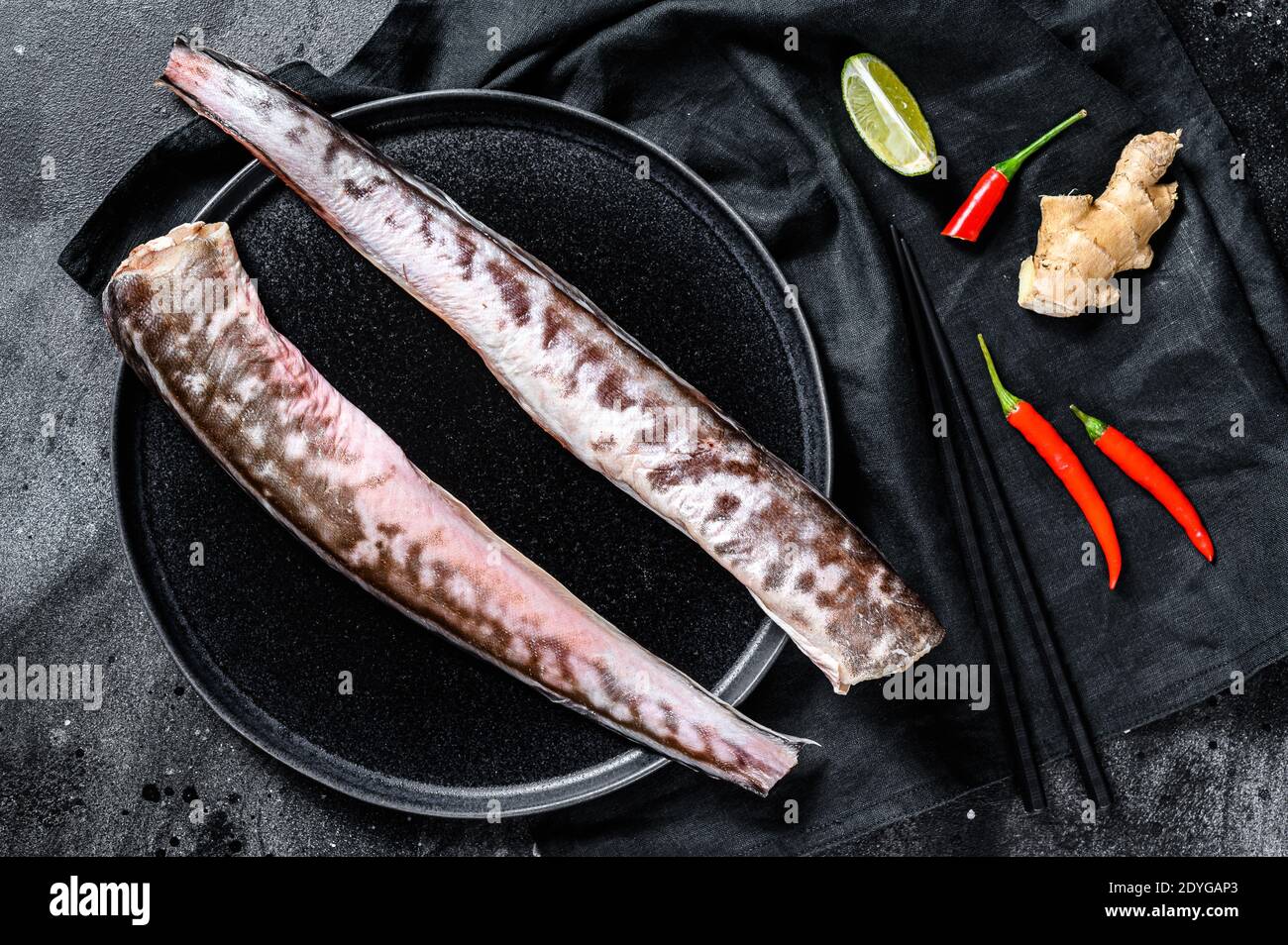 Raw sea eel fish with cooking ingredients, lime, ginger chili pepper. Black background. Top view. Stock Photo