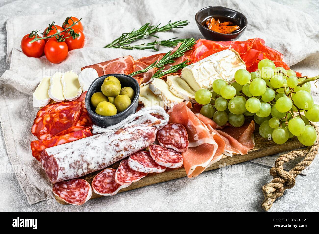 Italian antipasto, wooden cutting board with prosciutto, ham, parma, goat and Camembert cheese, olives, grapes. antipasti. Gray background. Top view Stock Photo