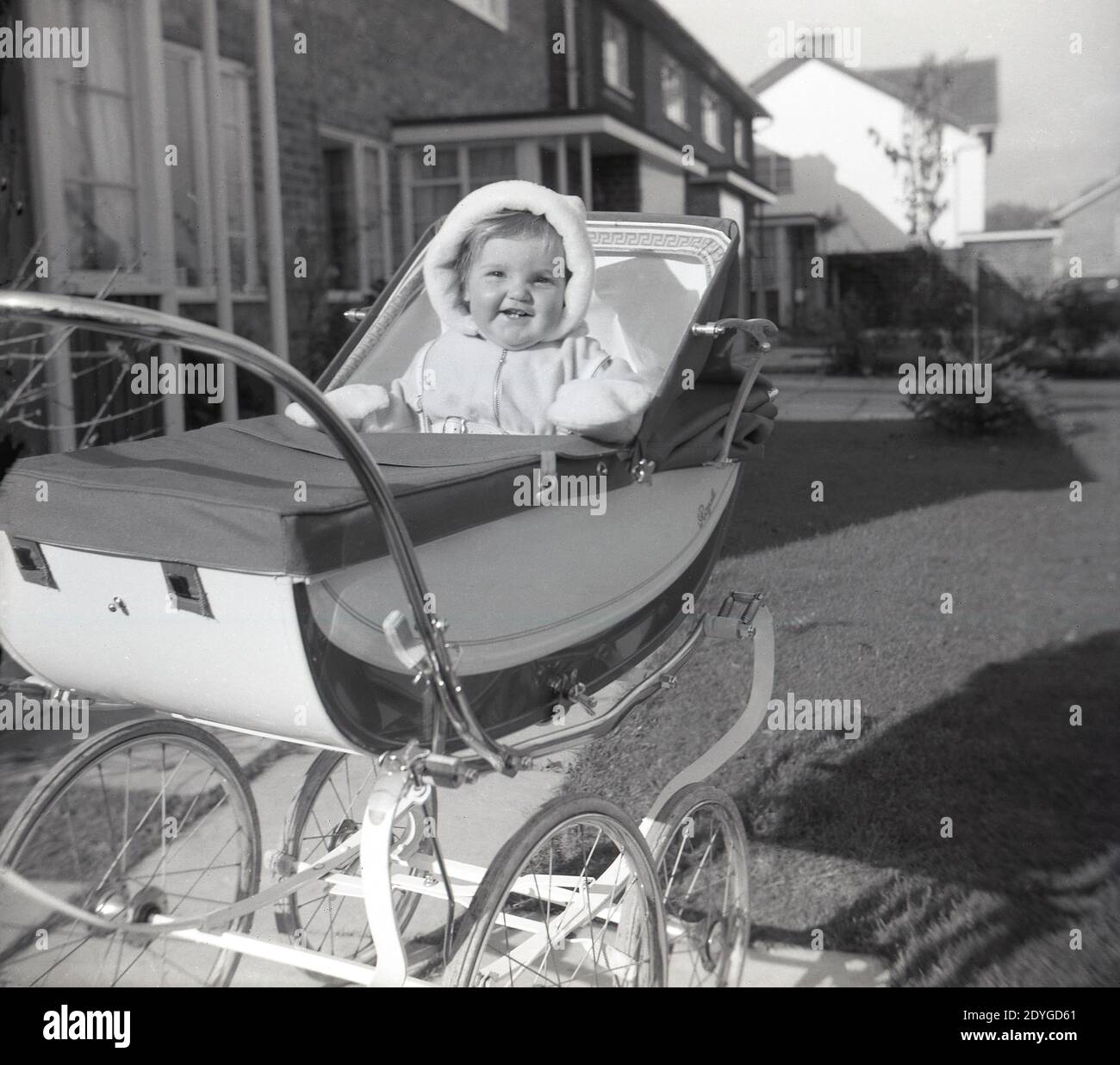 1960s, historical, outside in the fresh air, an infant child sitting in an elegant two-tone coach-built pram or baby carriage of the era, a Royale, Made in England. With its high, spring-suspension body and large spoke wheels behind smaller wheels, the Royale of London was a luxury coach-built pram. Royale was the brand name of the 'Royale Baby Carriage Co' of Nunhead Grove, London, founded in 1930 by brothers Alf & Frank Saward. Beautiful baby carriages such as the Royale declined in use from the 1970s as cheaper, lighter prams and more convenient collapsible prams took over the market. Stock Photo