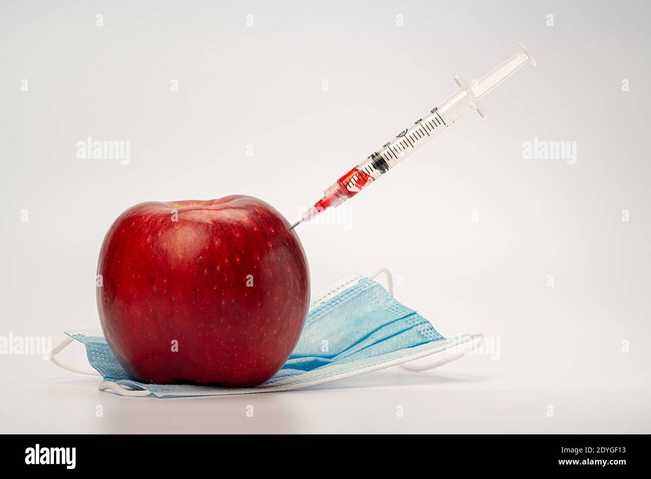 A syringe is injecting an apple, symbolic of vaccination and medical treatment Stock Photo