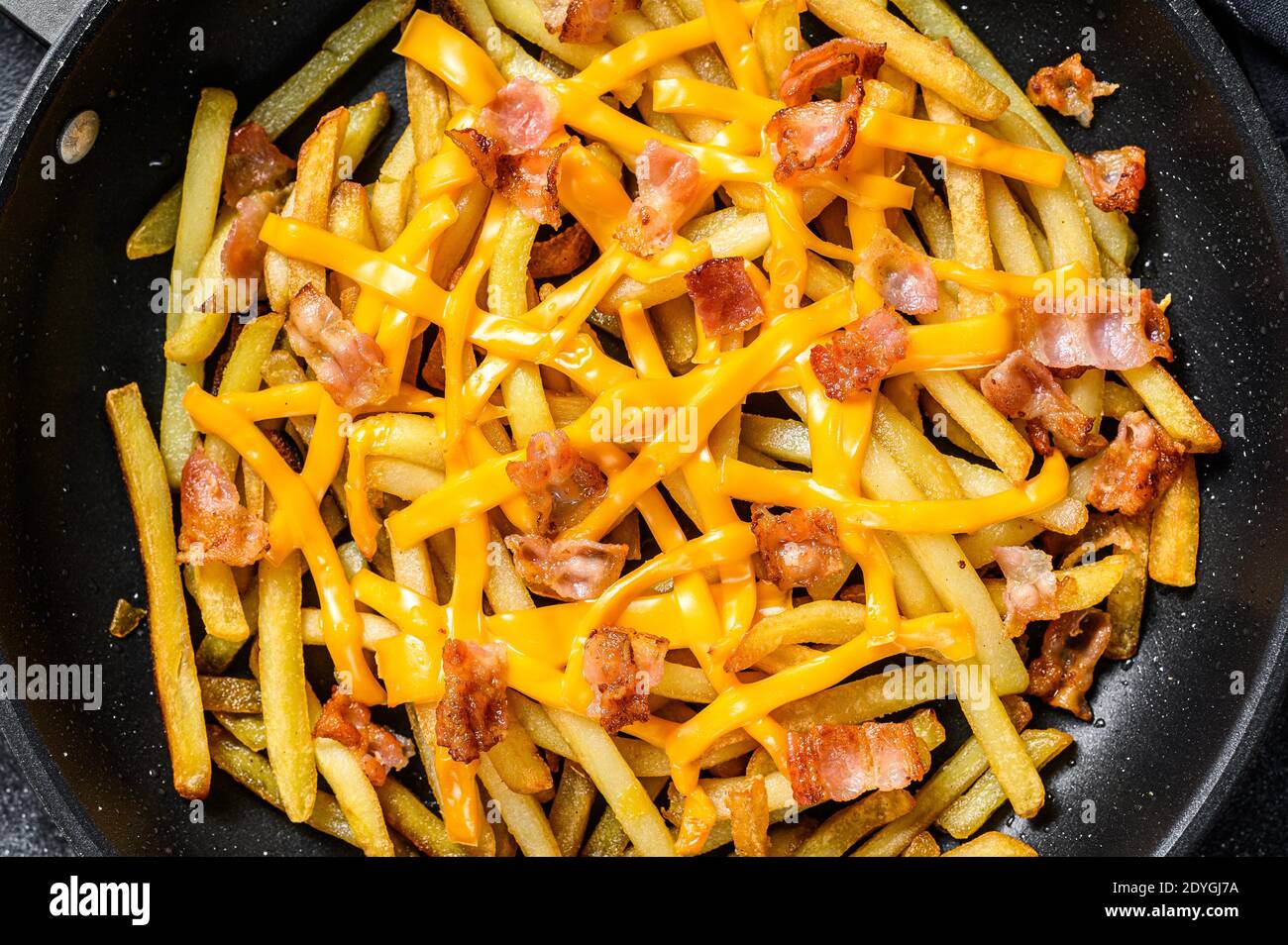 Golden French fries fried with cheddar cheese and bacon in a pan. Black