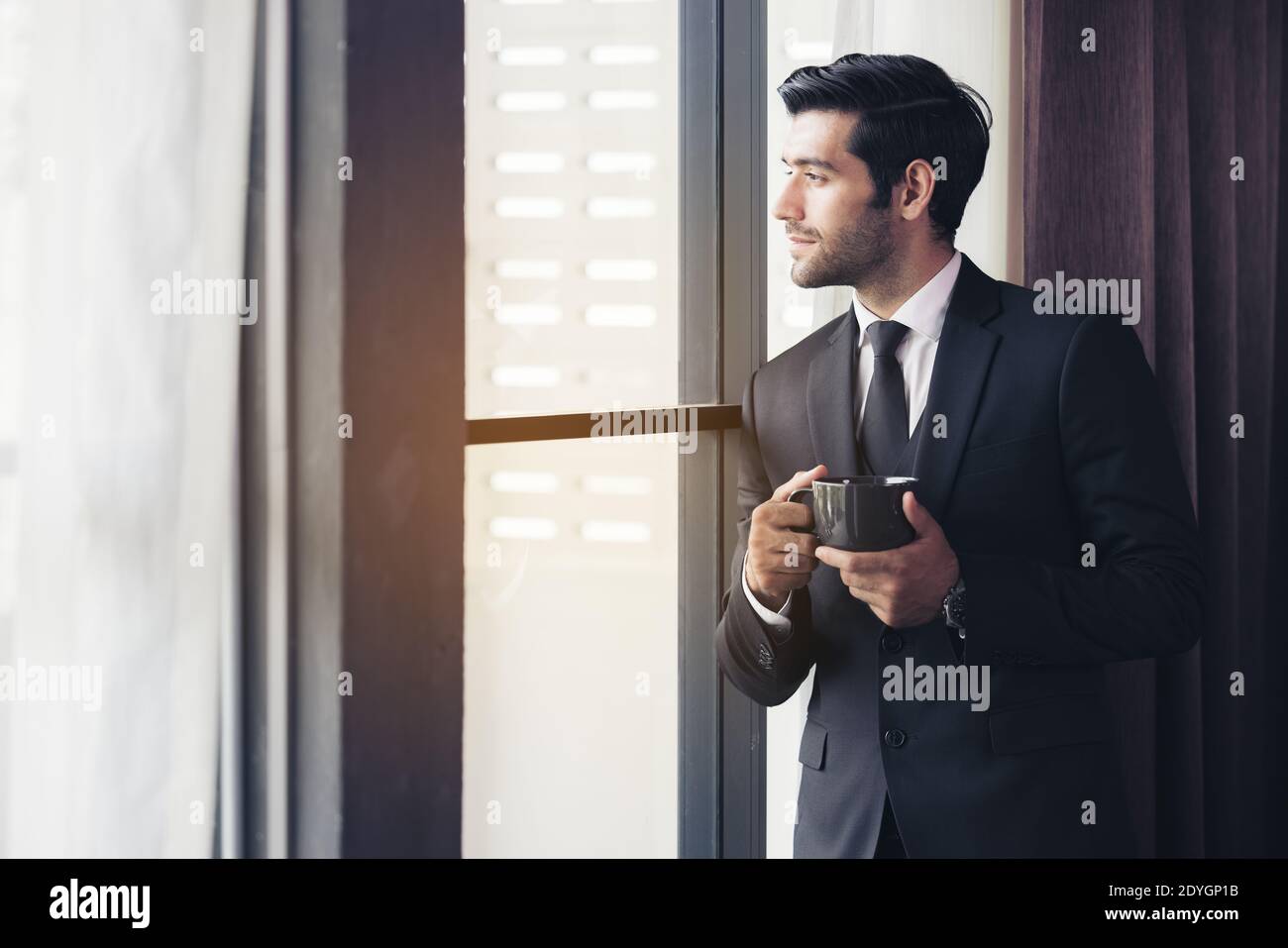 Thoughtful businessman drinking coffee, looking through window at big modern city, having break, deep in thoughts, enjoying view, waiting for meeting Stock Photo