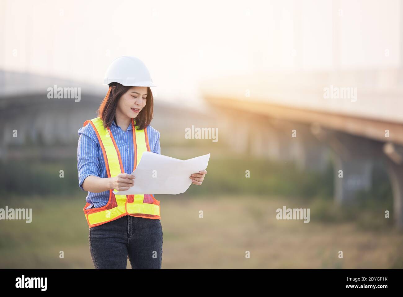 Beautiful Asian female engineer in white safety hard hat doing job at construction site outside office. Idea for modern working woman hightway road Stock Photo