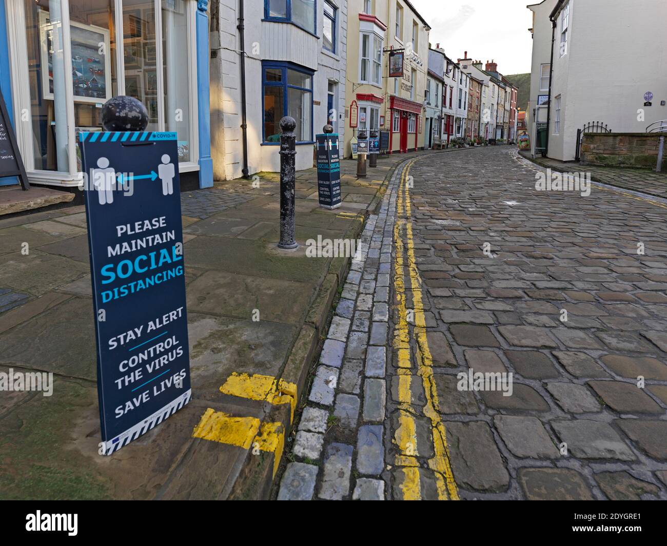 Covid-19 social distancing reminder signs on street bollards in the rural North Yorkshire town of Staithes Stock Photo