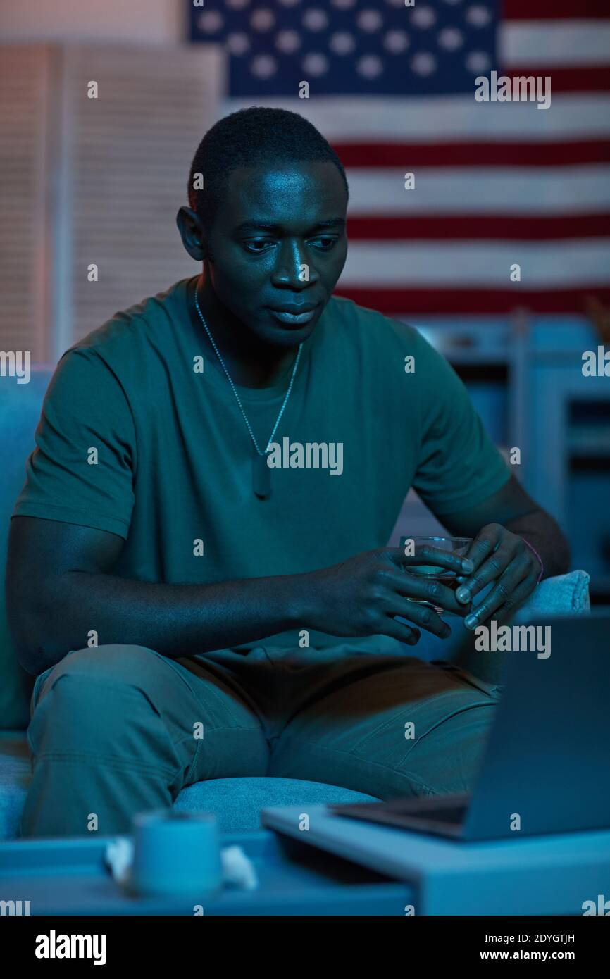 African young man drinking alcohol and watching something on laptop while sitting on the sofa Stock Photo