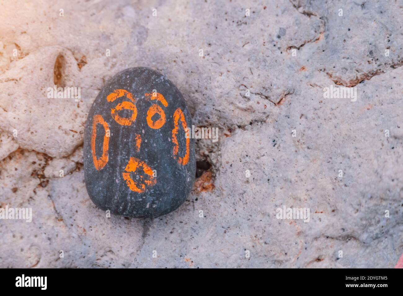 Grey Pebble with a orange painted smiling face. On a small stone is an image of a happy face. Concept: joy, happiness, positive, kindness. Stock Photo
