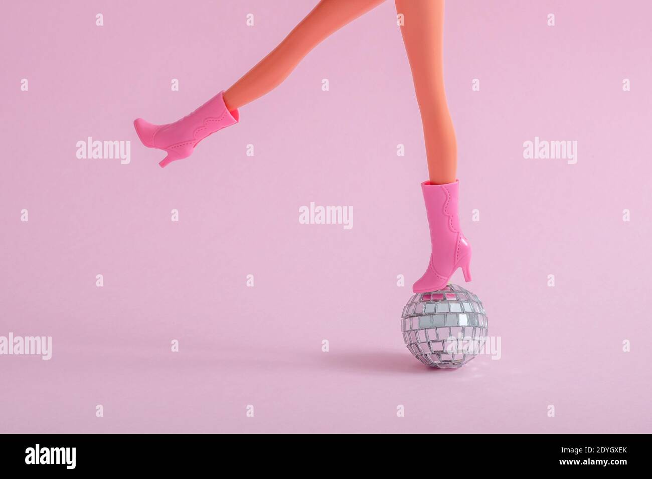 Plastic doll feet on a small disco ball on a pink background Stock