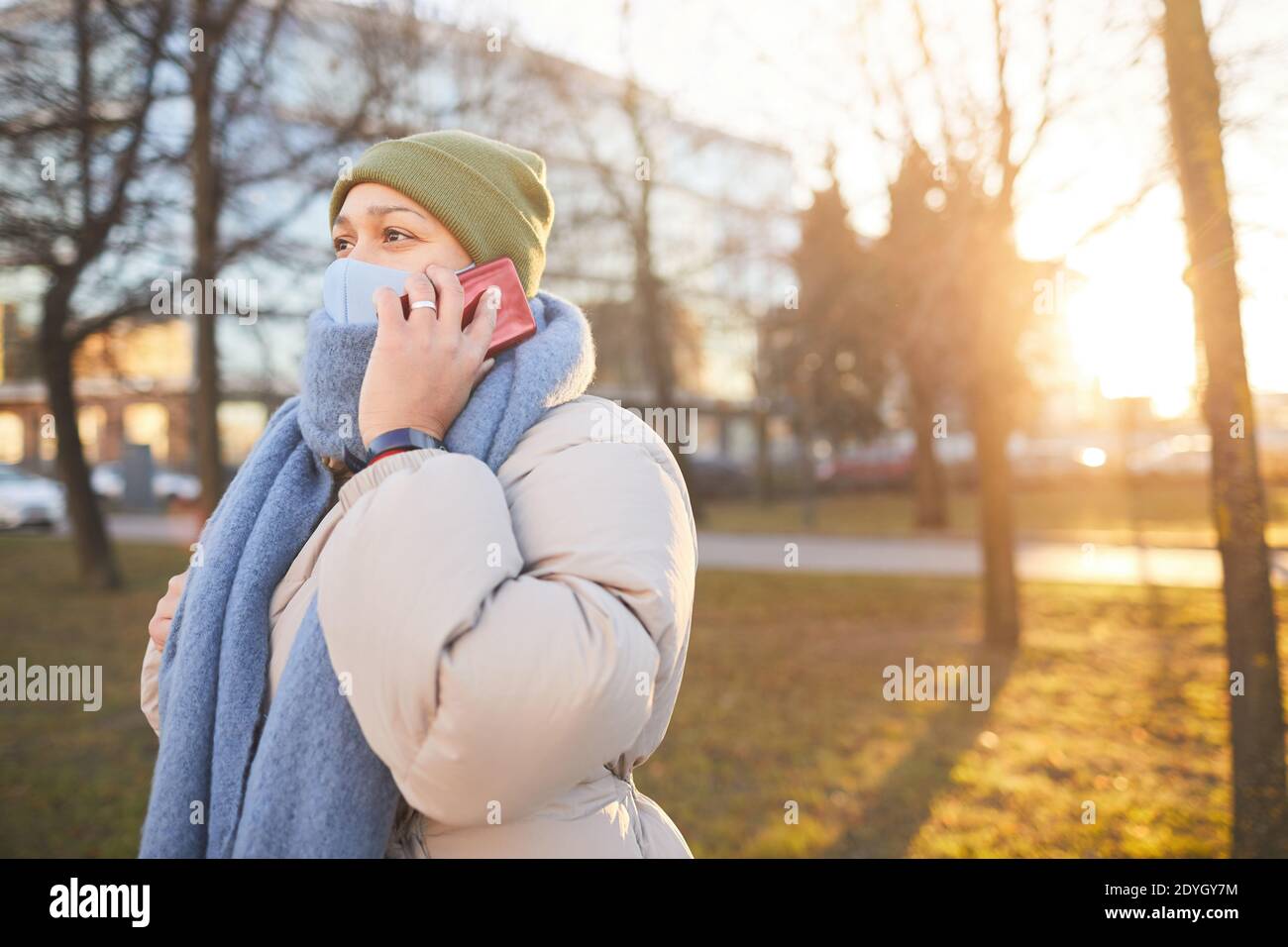 Young woman in protective mask talking on the phone while walking in the city Stock Photo