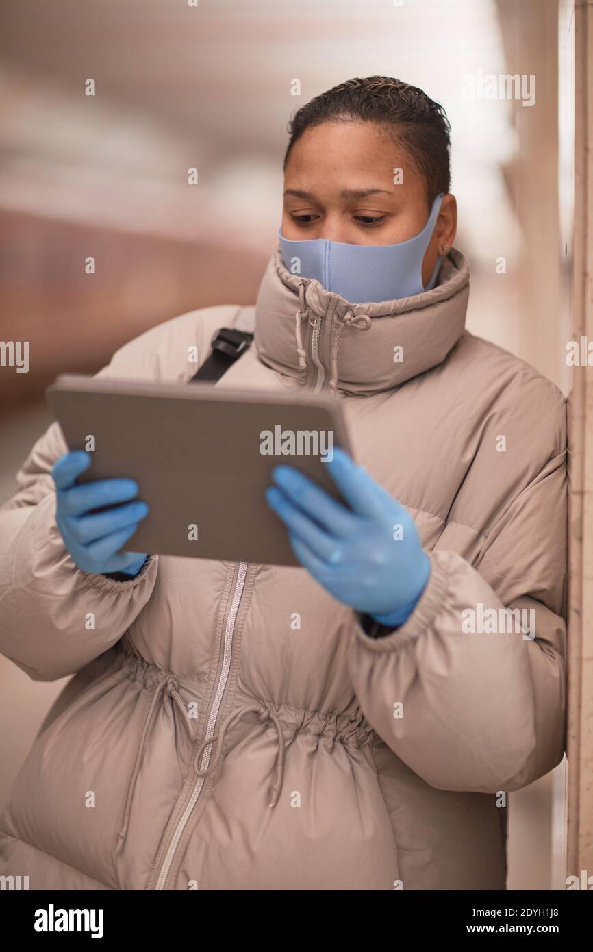 Young woman in mask and in protective gloves using digital tablet while waiting for the train Stock Photo