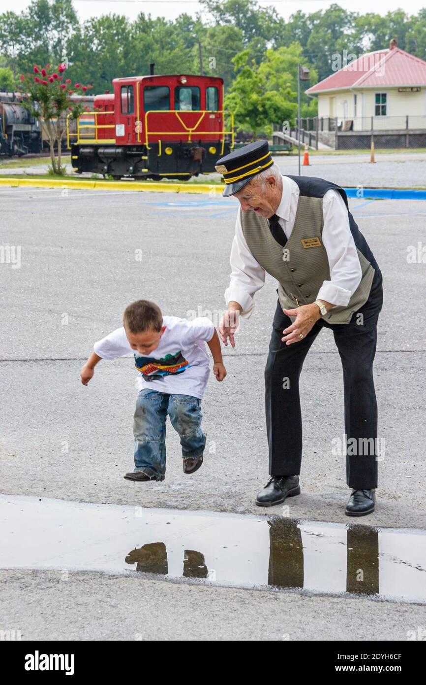 Alabama Calera Heart of Dixie Railroad Museum,senior man male conductor's uniform boy kid child,jumps jumping puddle, Stock Photo