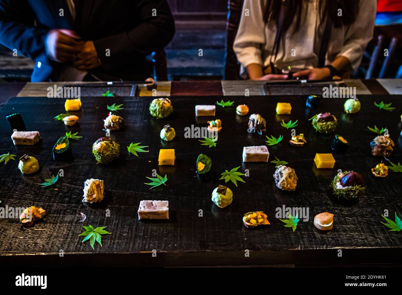 Kaiseki bites are artfully scattered across maple leaves and dark wood – the chirashi-mori plating technique on a hassun appetizer platter at chef Atsuko Kato's Rakan restaurant, Izu Peninsula, Japan. Stock Photo