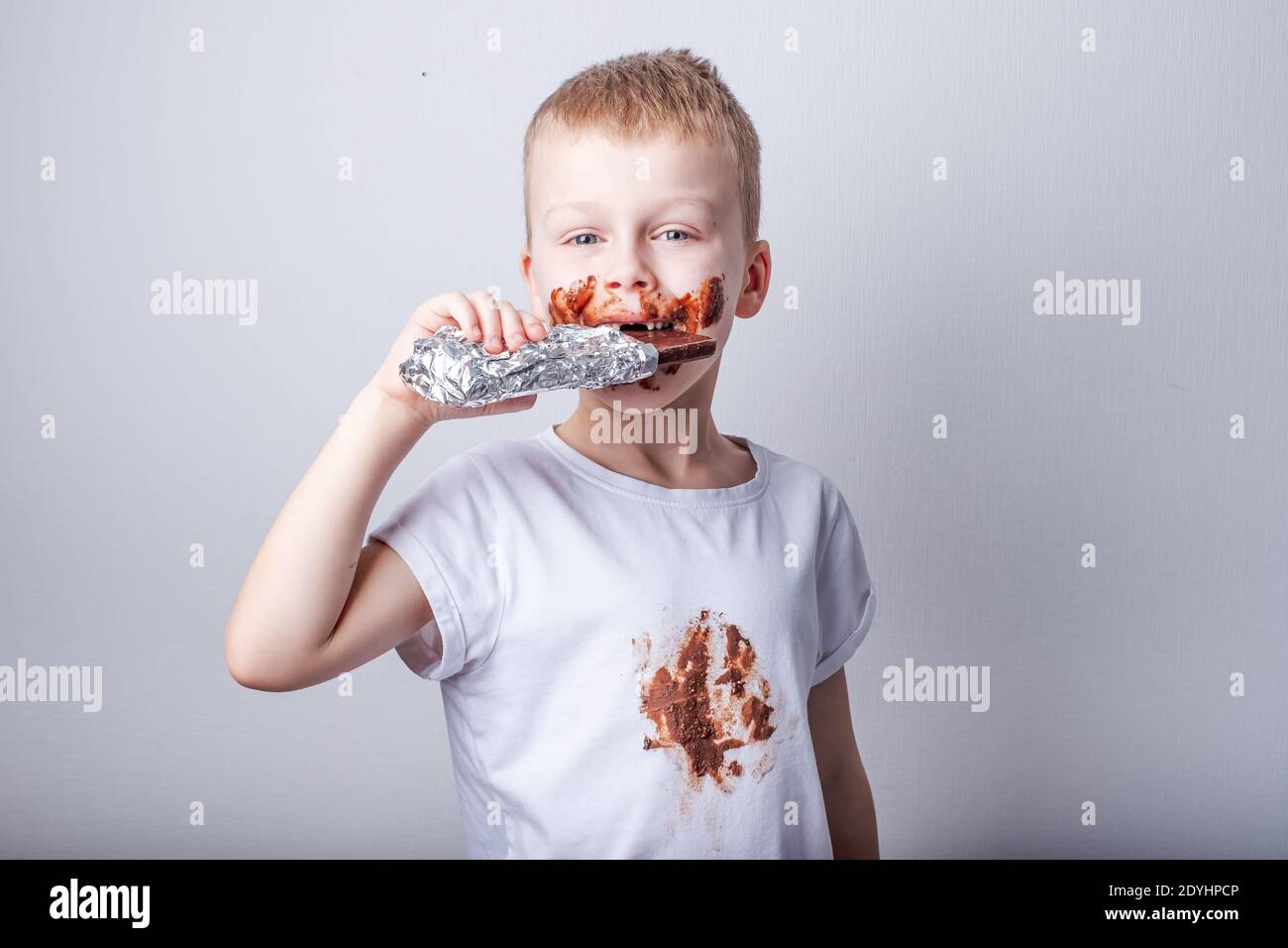 Boy eating a bar of chocolate in his grin and smeared clothes. High quality photo Stock Photo