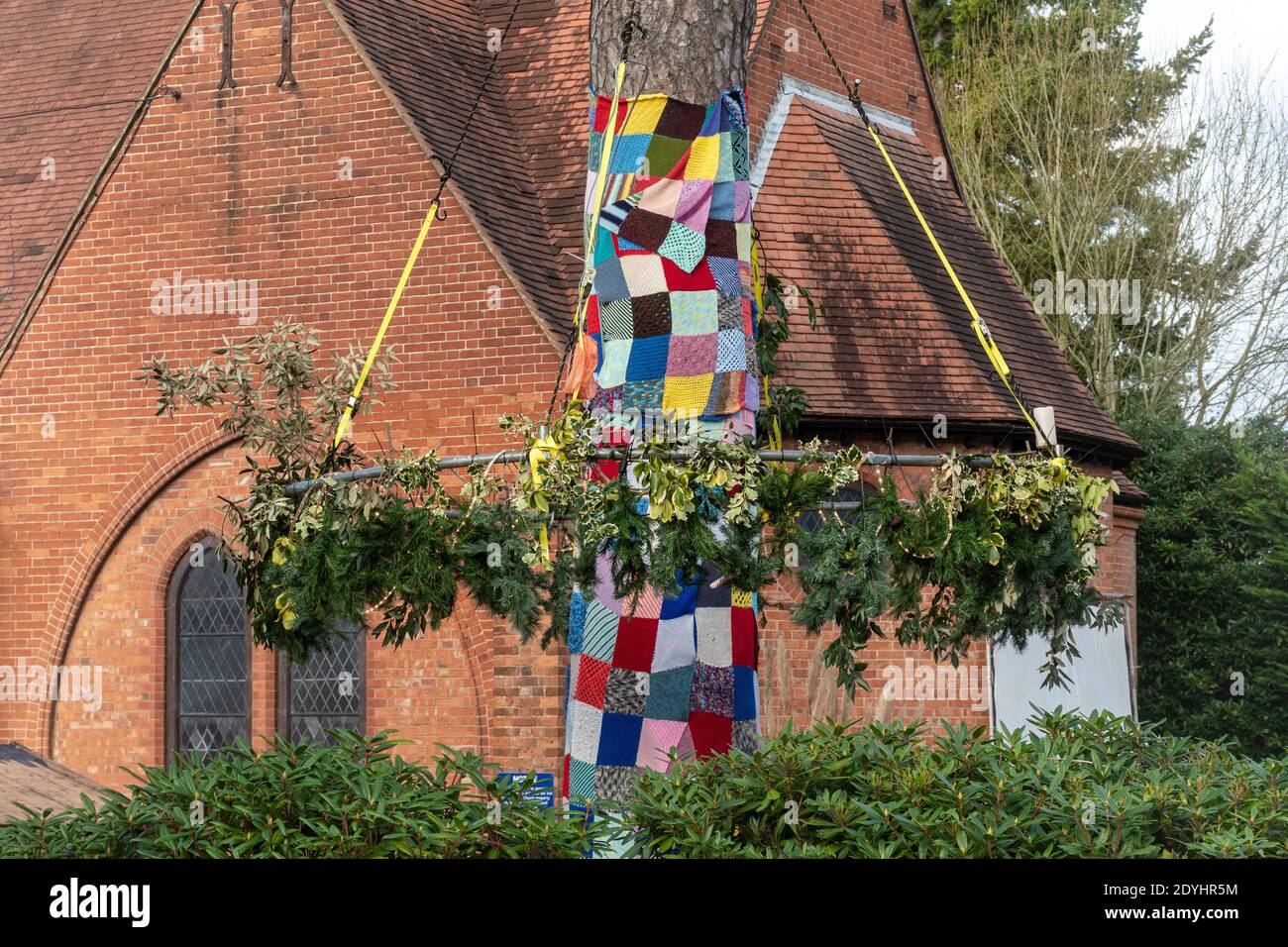 Natural christmas decorations made with holly and pine around a tree with a blanket made of crocheted squares outside St Mary's Church, Ash Vale, UK Stock Photo