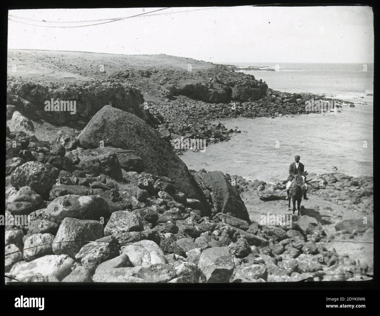 Landscape view beside the coast with a moai fallen on its back towards the sea and a man sitting on a horse for scale; Ahu Tetenga OcG.T.1498 Mana Expedition to Easter Island Stock Photo