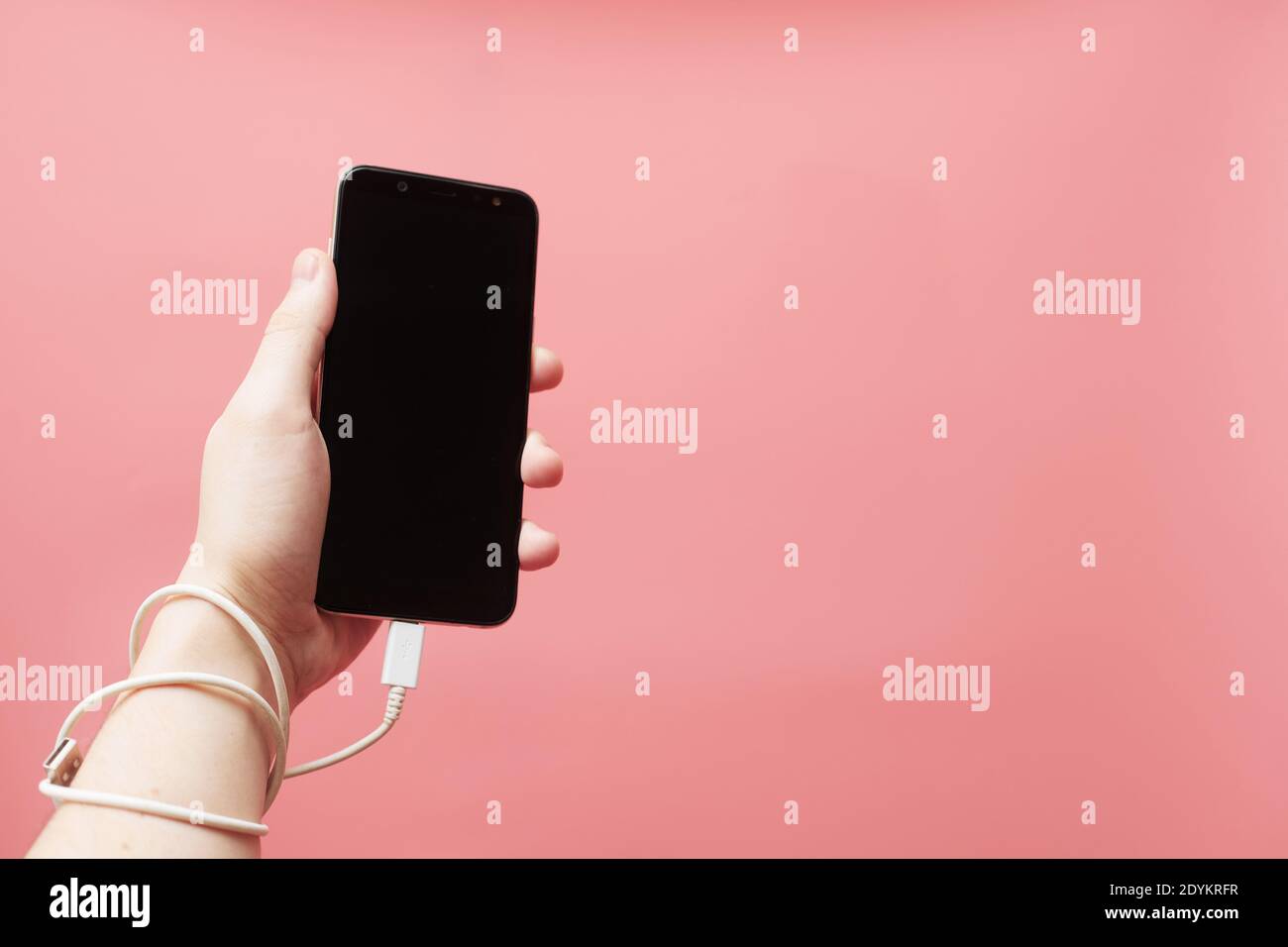 Phone addiction, social networks concept, smartphone tied to hand with wire on pink background Stock Photo