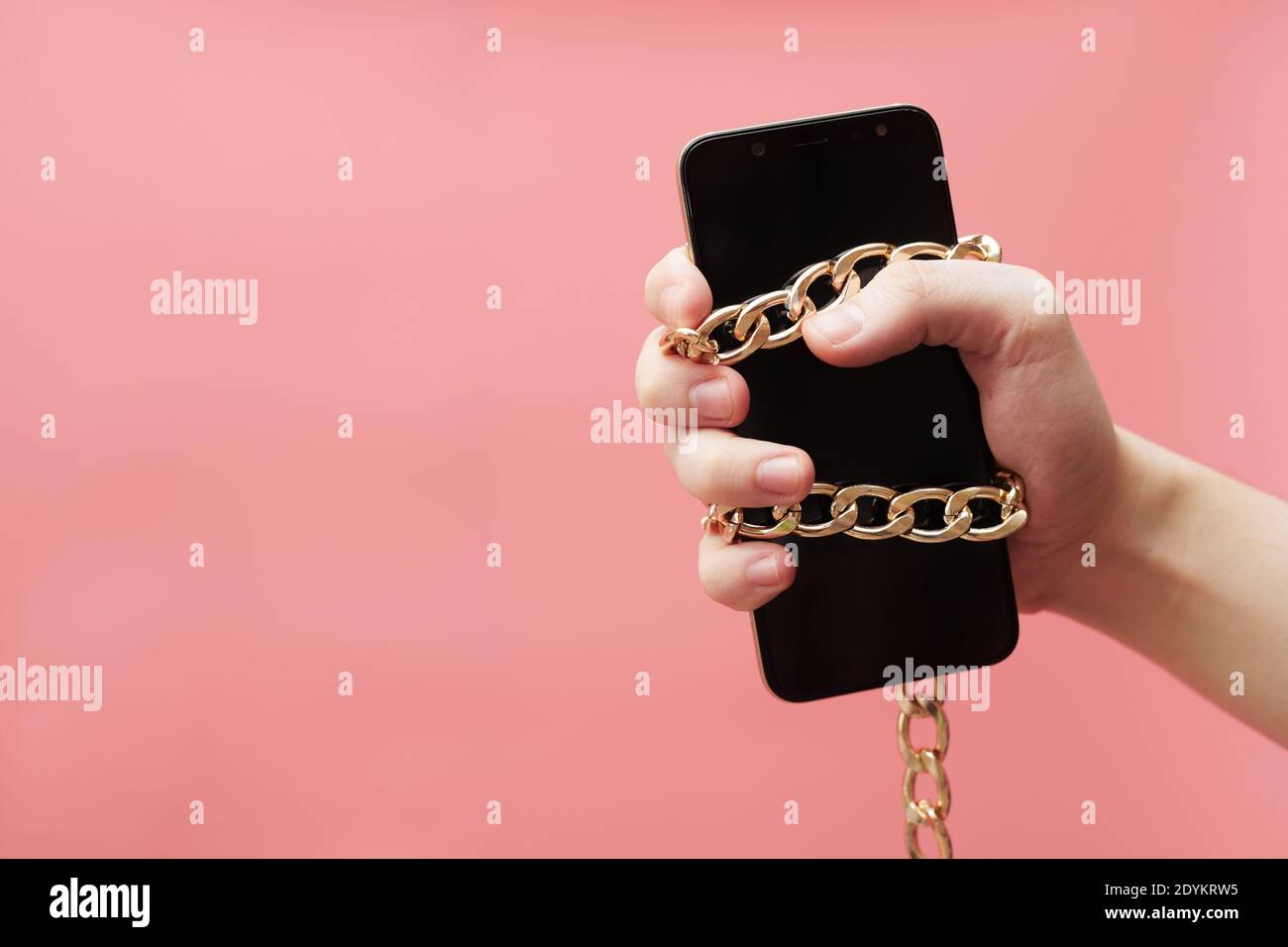 Phone addiction, social networks concept, tied to hand with a chain smartphone on a pink background Stock Photo
