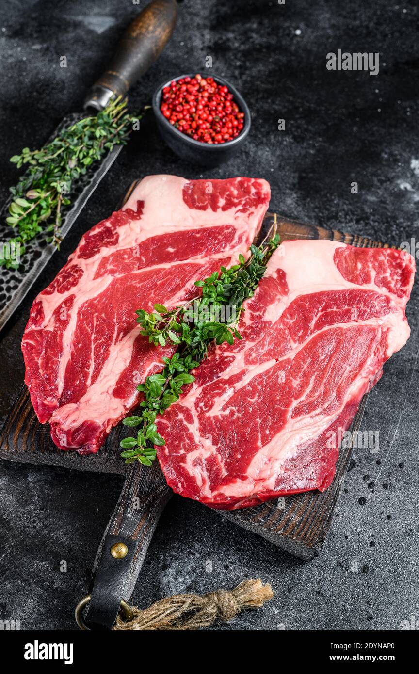 Raw chuck eye roll steaks premium beef meat on a cutting board. Black