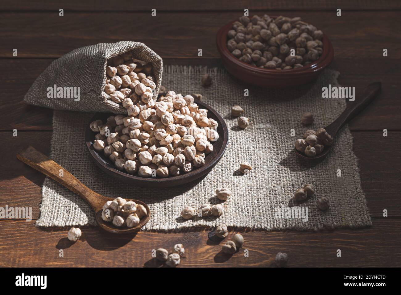 Spilled chickpeas on a wooden plate, wooden spoons on a wooden base. Stock Photo