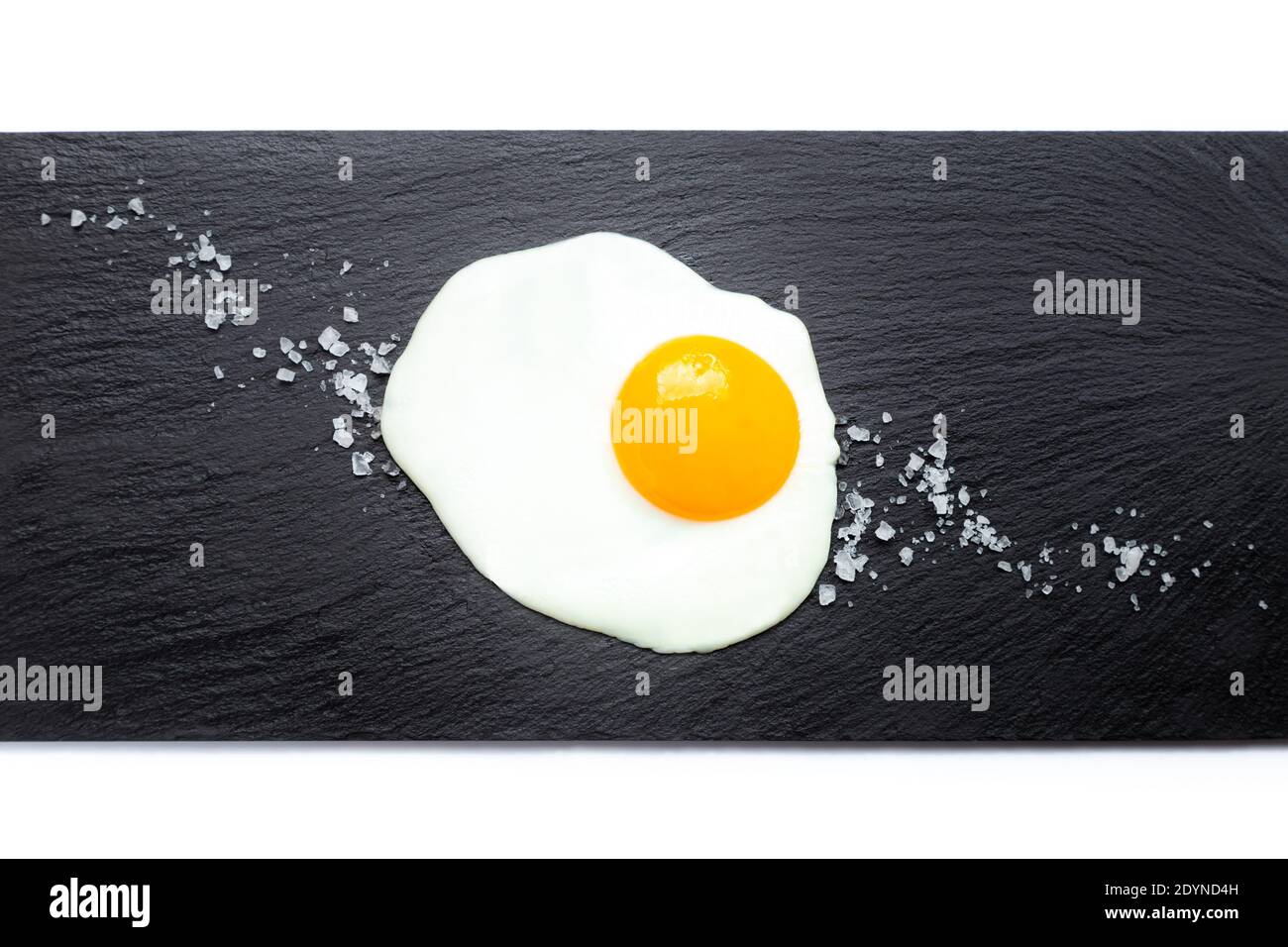 Fried egg on slate plate with salt on white background. Cooking and food concept. Stock Photo