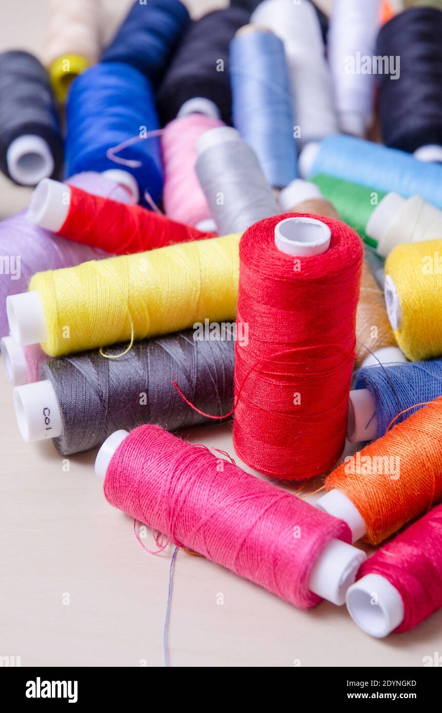 Flat lay of spools with colorful threads on wooden desk or table, home crafting, indoors, sewing kit, close-up Stock Photo