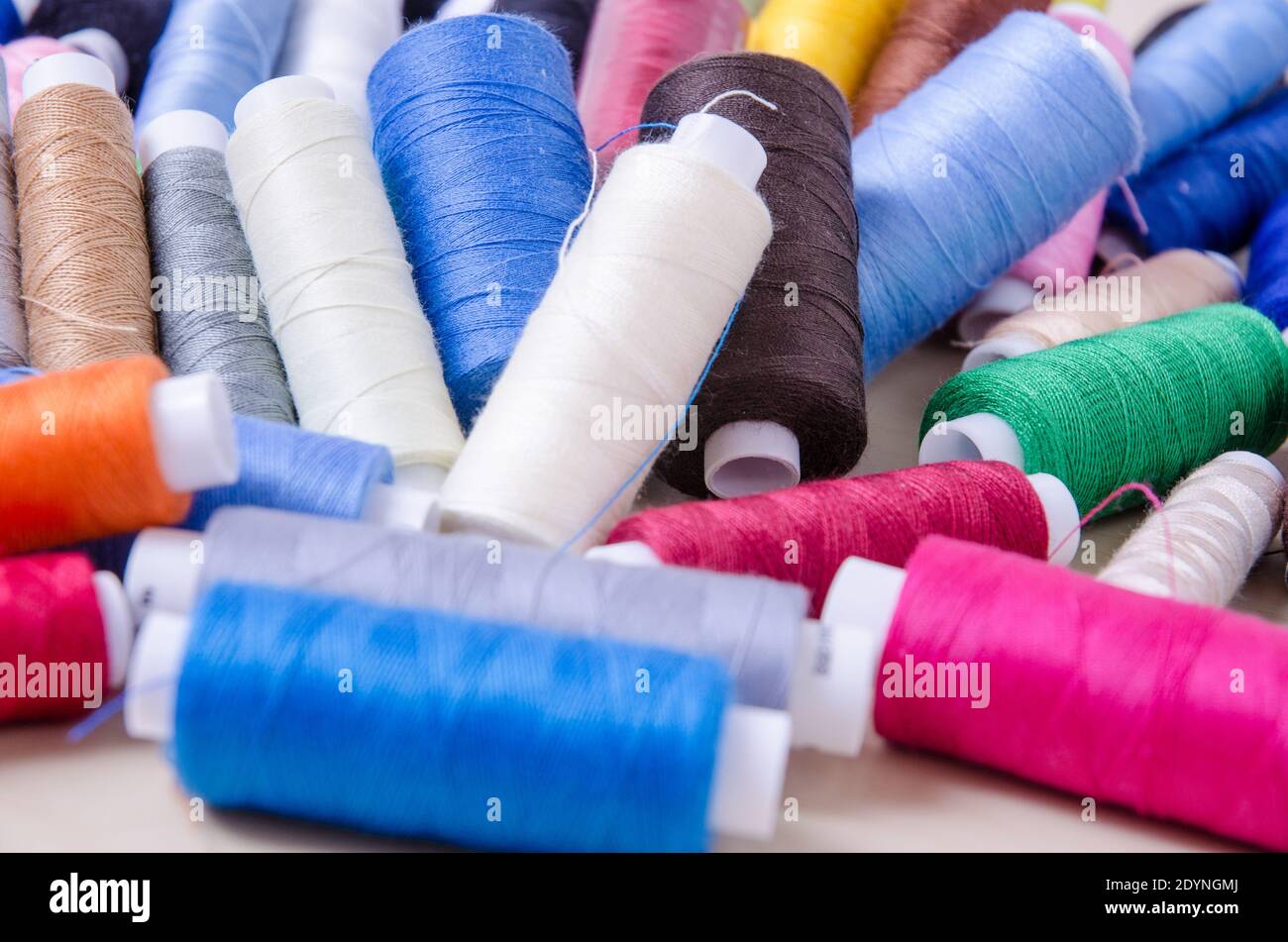 Flat lay of spools with colorful threads on wooden desk or table, home crafting, indoors, sewing kit, close-up Stock Photo