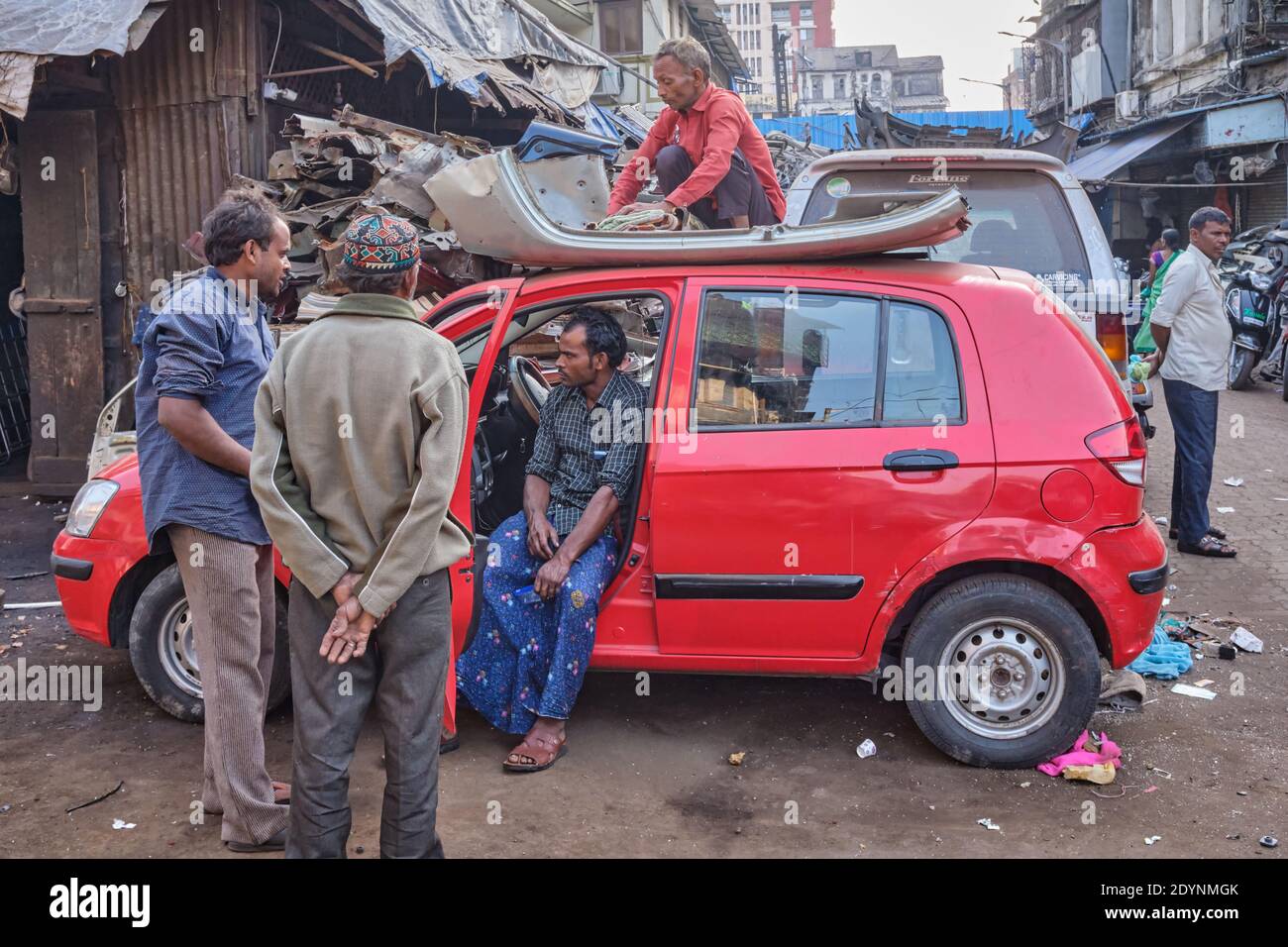 Dismantling an old car, the employee of a junk shop sits on the roof of another discarded car; Chor Bazar / Bazaar (Thieves' Market), Mumbai, India Stock Photo