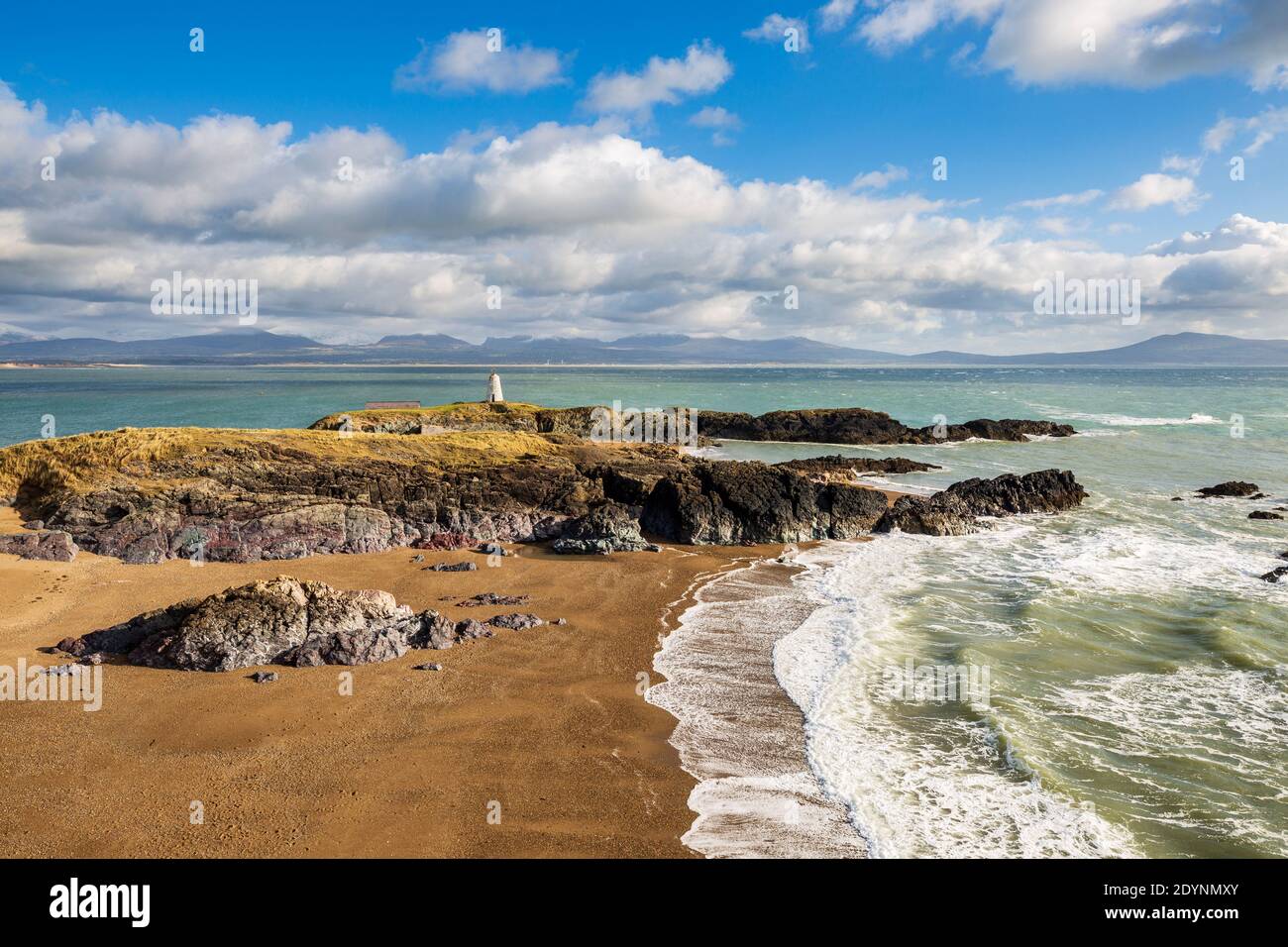 A view of Twr Bach and the snow capped Snowdonia mountains across Porth Twr Mawr on Llanddwyn island, Anglesey Stock Photo