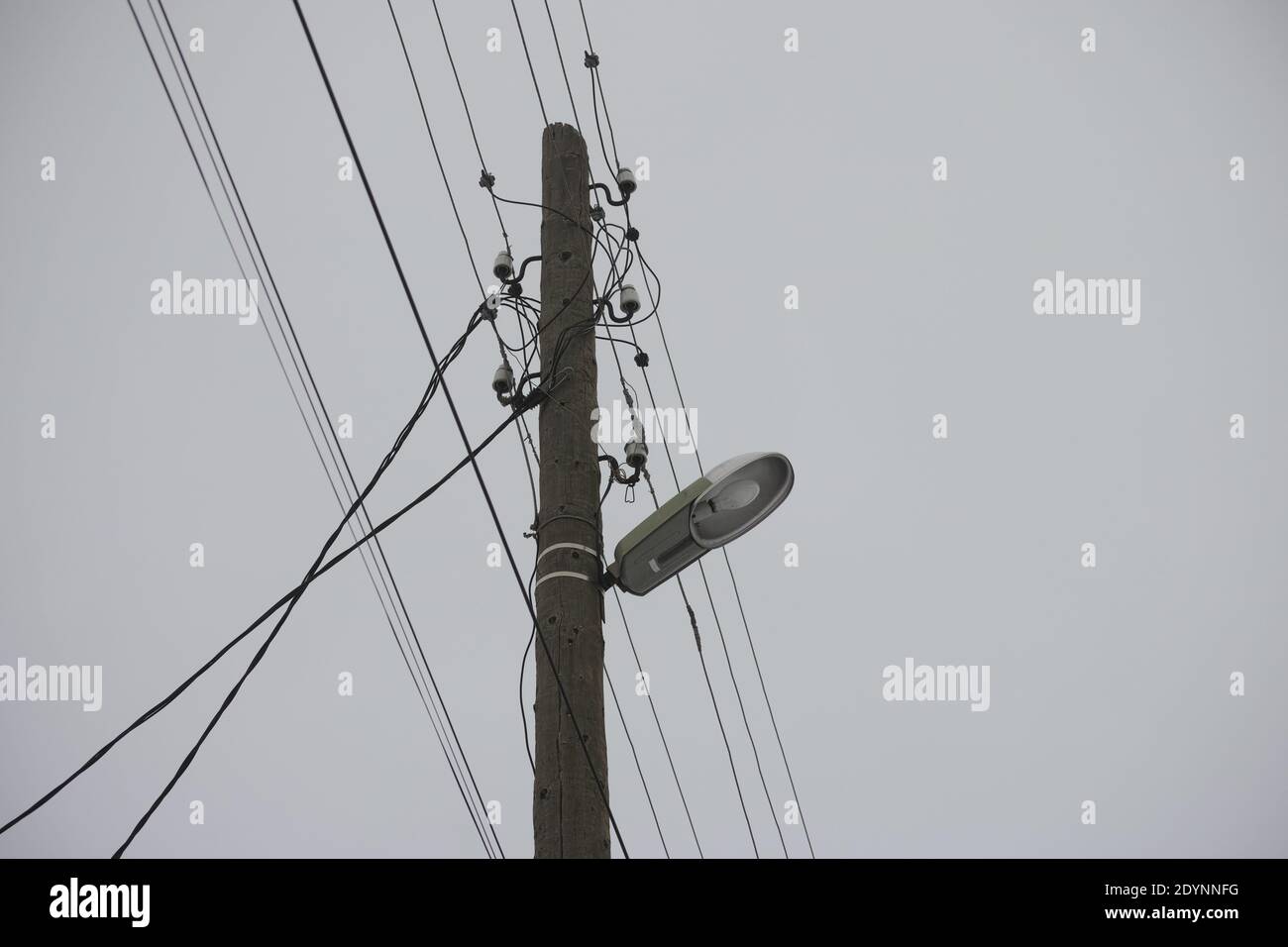 An old electric wooden pole with a lamp and electricity cables hanging on it. Stock Photo