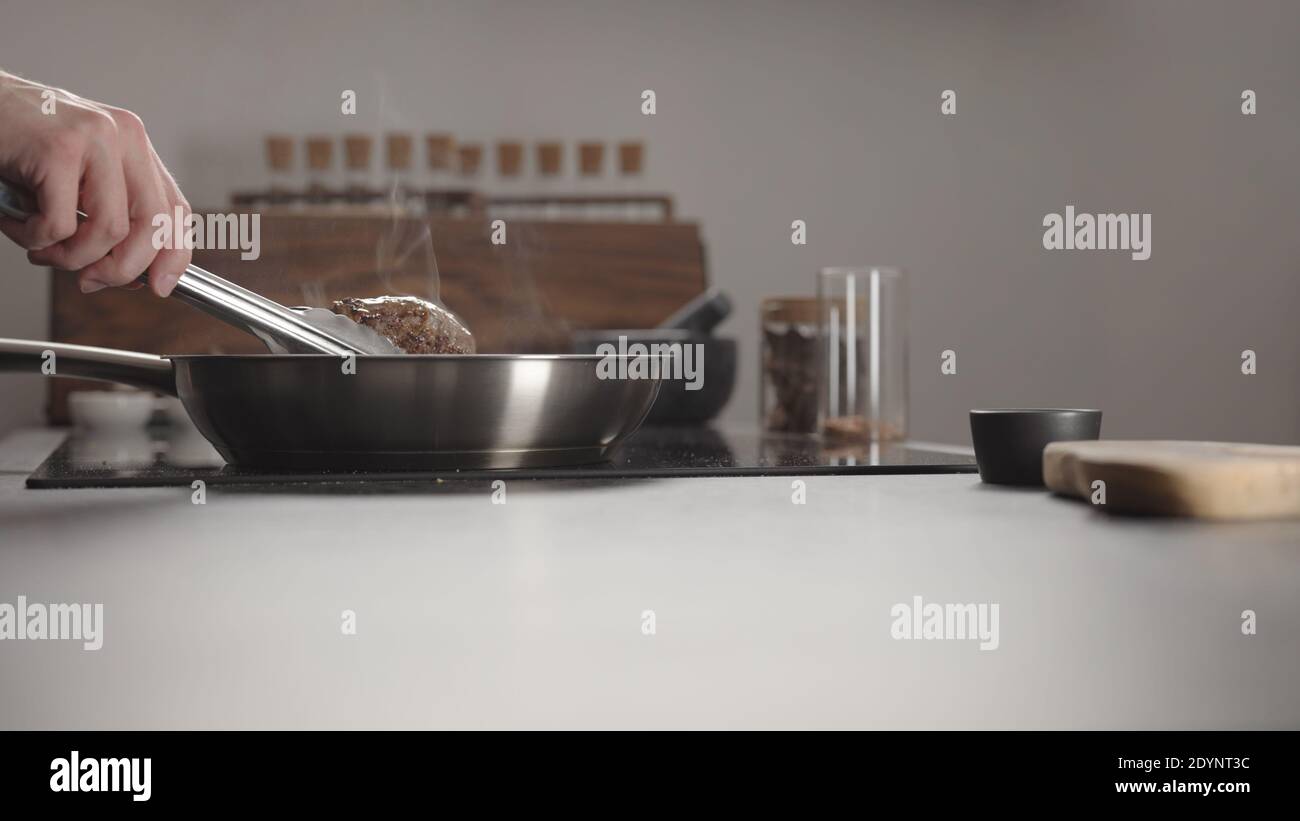 Man frying beef steak searing side on steel pan on electric hob on