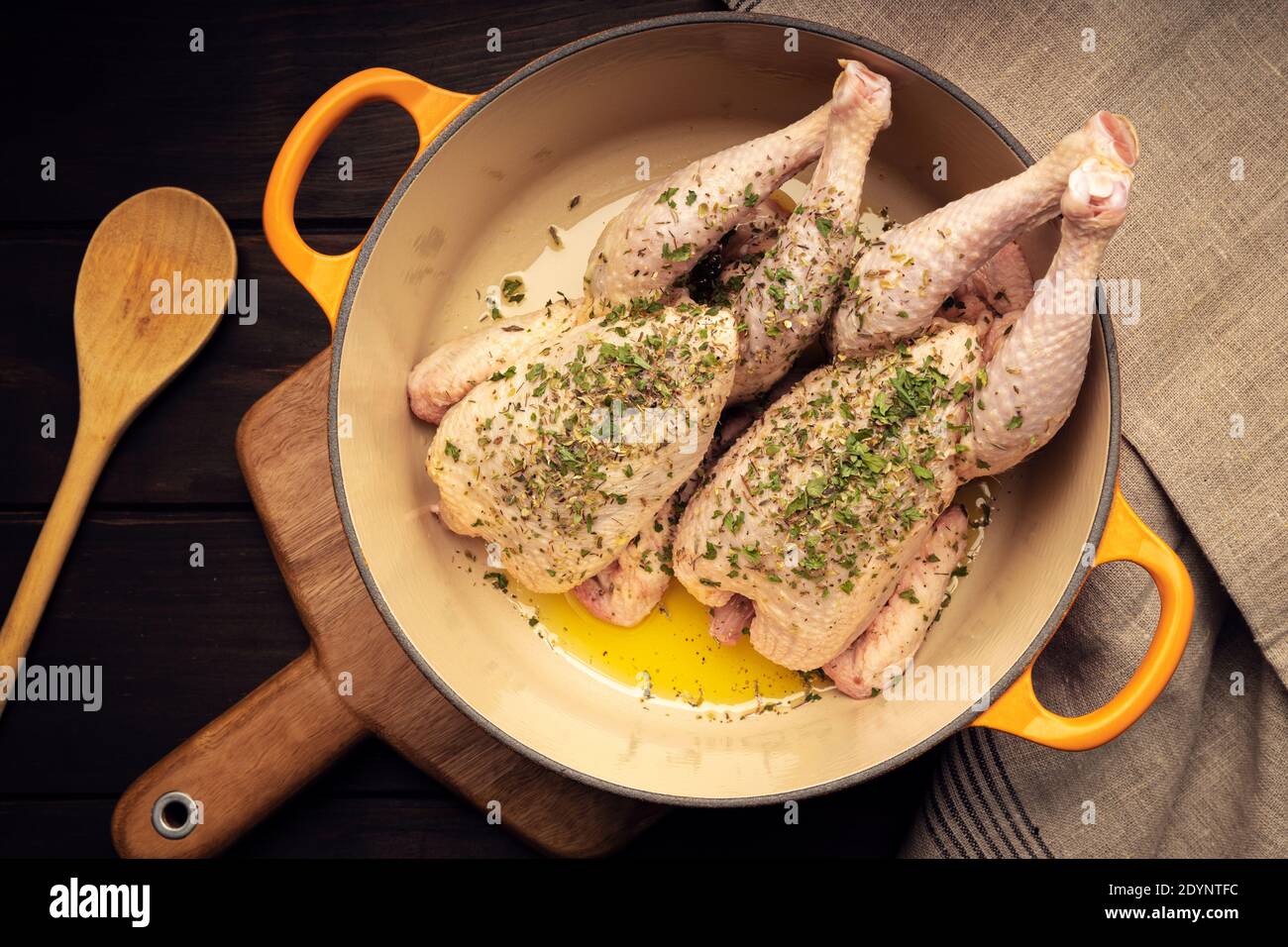 Uncooked Spicy chickens in cast iron cooking pot on wooden table. Spanish traditional recipe. Top view Stock Photo