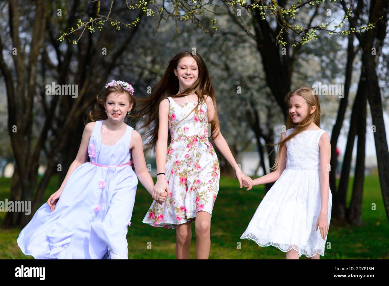 Three adorable girls in dresses hold hands in a circle holding hands ...
