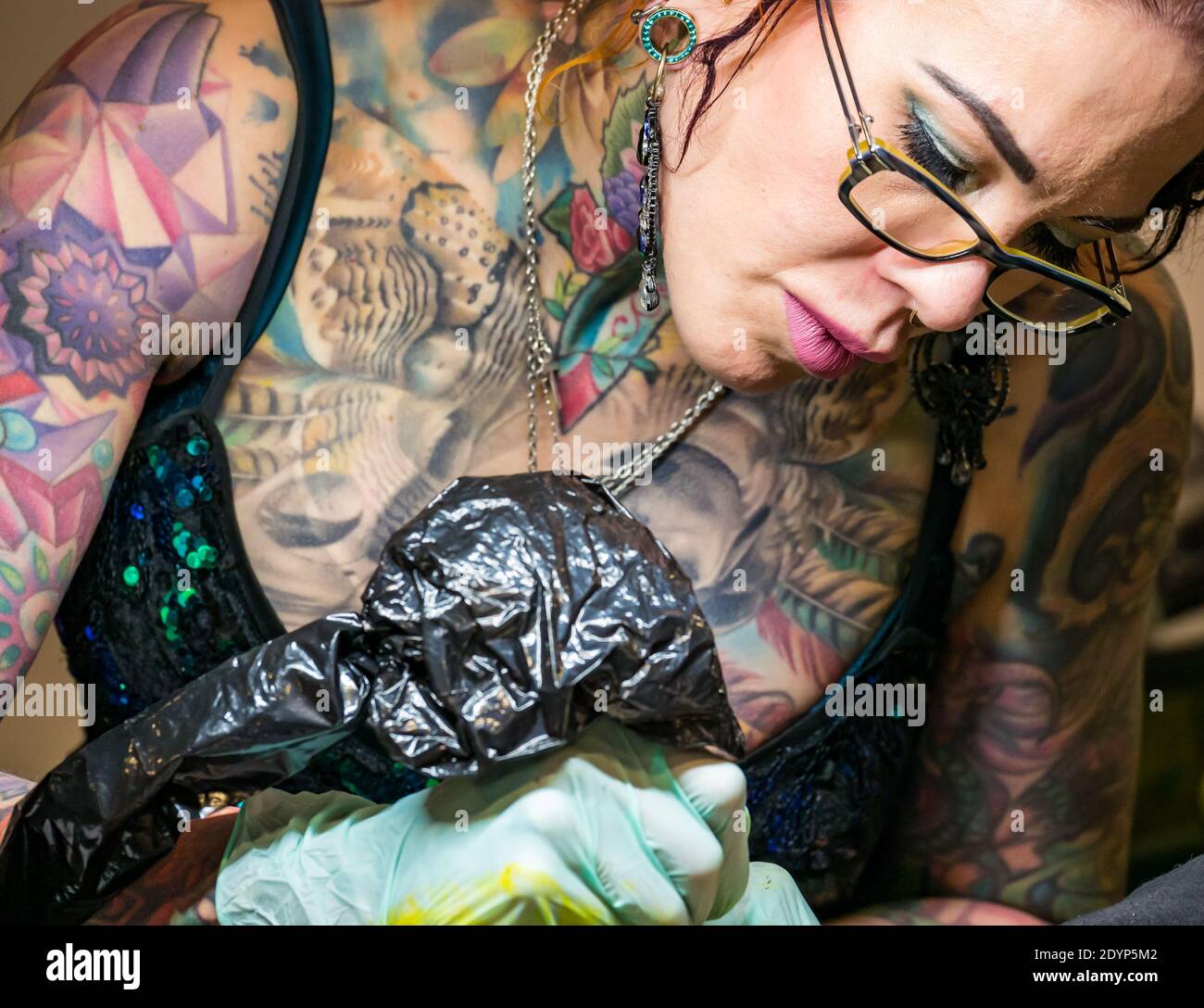 Female tattooist or tattoo artist covered in tattoos at work, Scotland, UK Stock Photo