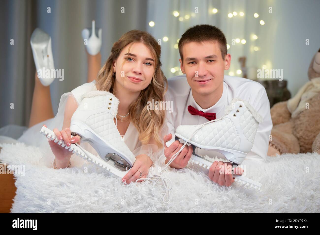Beautiful young couple lie on the bed with figure skates and look at the camera. Stock Photo