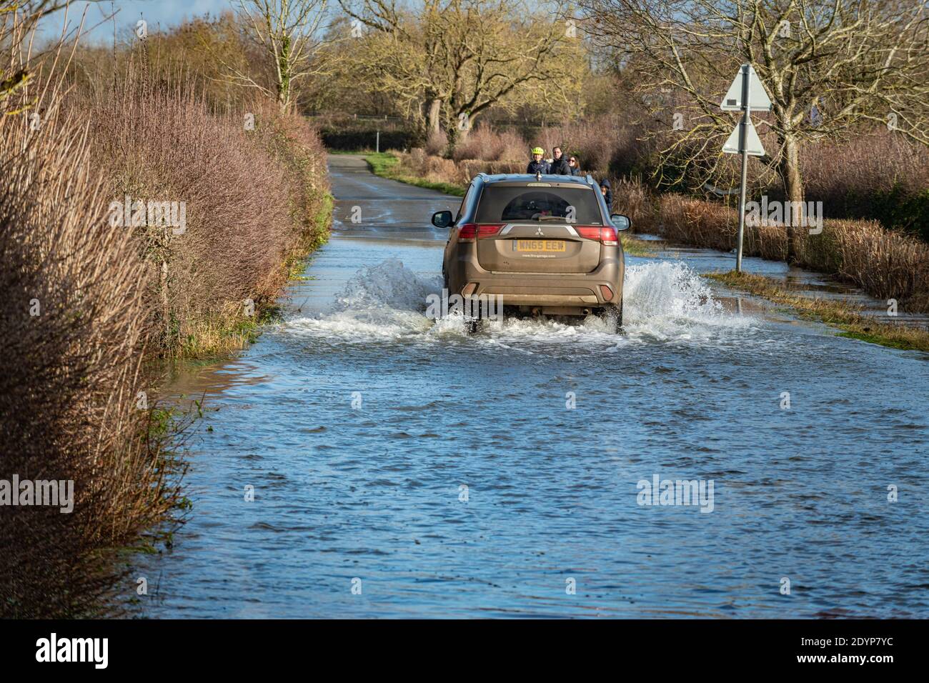 Wytham, Oxfordshire, UK. 27 December, 2020. Cars drive through the flooded road from Wytham to Wolvercote. Flooding in Oxfordshire. Storm Bella brought even more rain to Oxfordshire causing flooding in low lying areas. Plenty of people are out exercising in the sunshine. Credit: Sidney Bruere/Alamy Live News Stock Photo