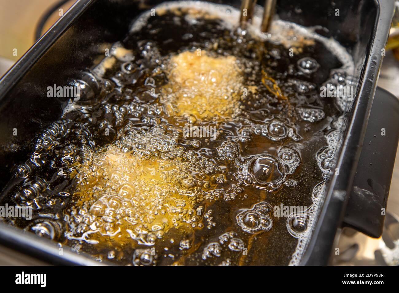A oil frier with food and chicken cooking in the frier Stock Photo