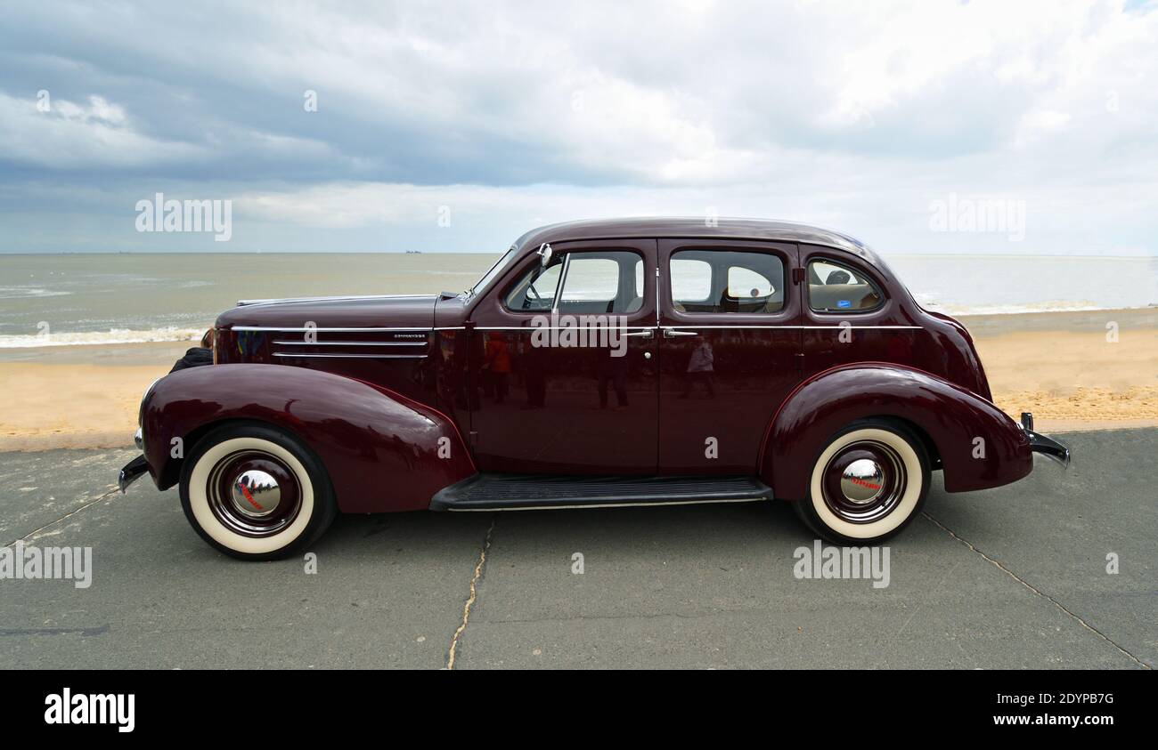 Classic Dark Red Studebaker  motor car parked  on seafront promenade beach and sea in background. Stock Photo