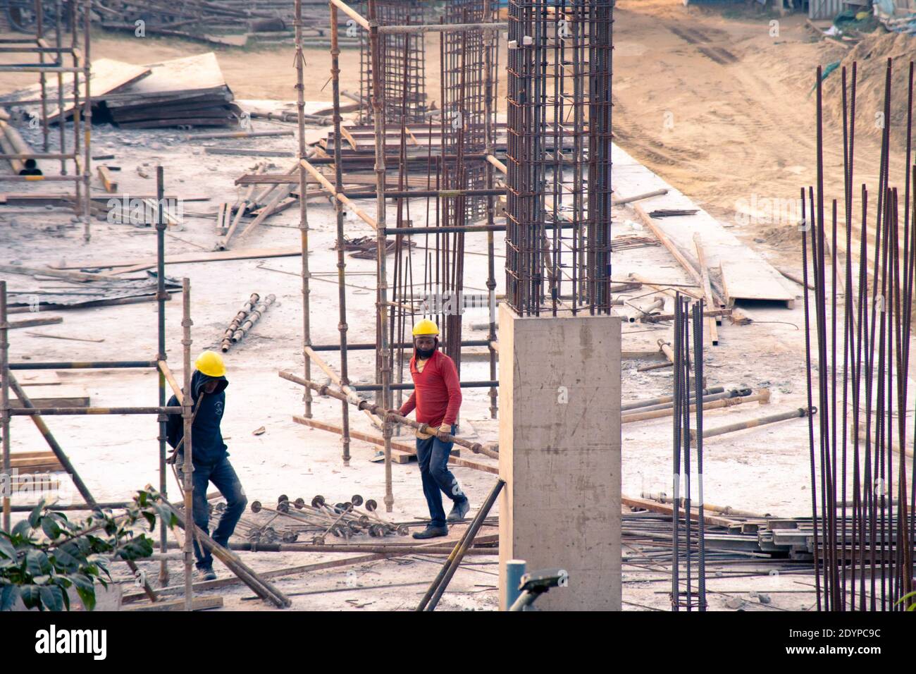 Indian construction site with man laborer in hoodie and helmet carrying equipment near half